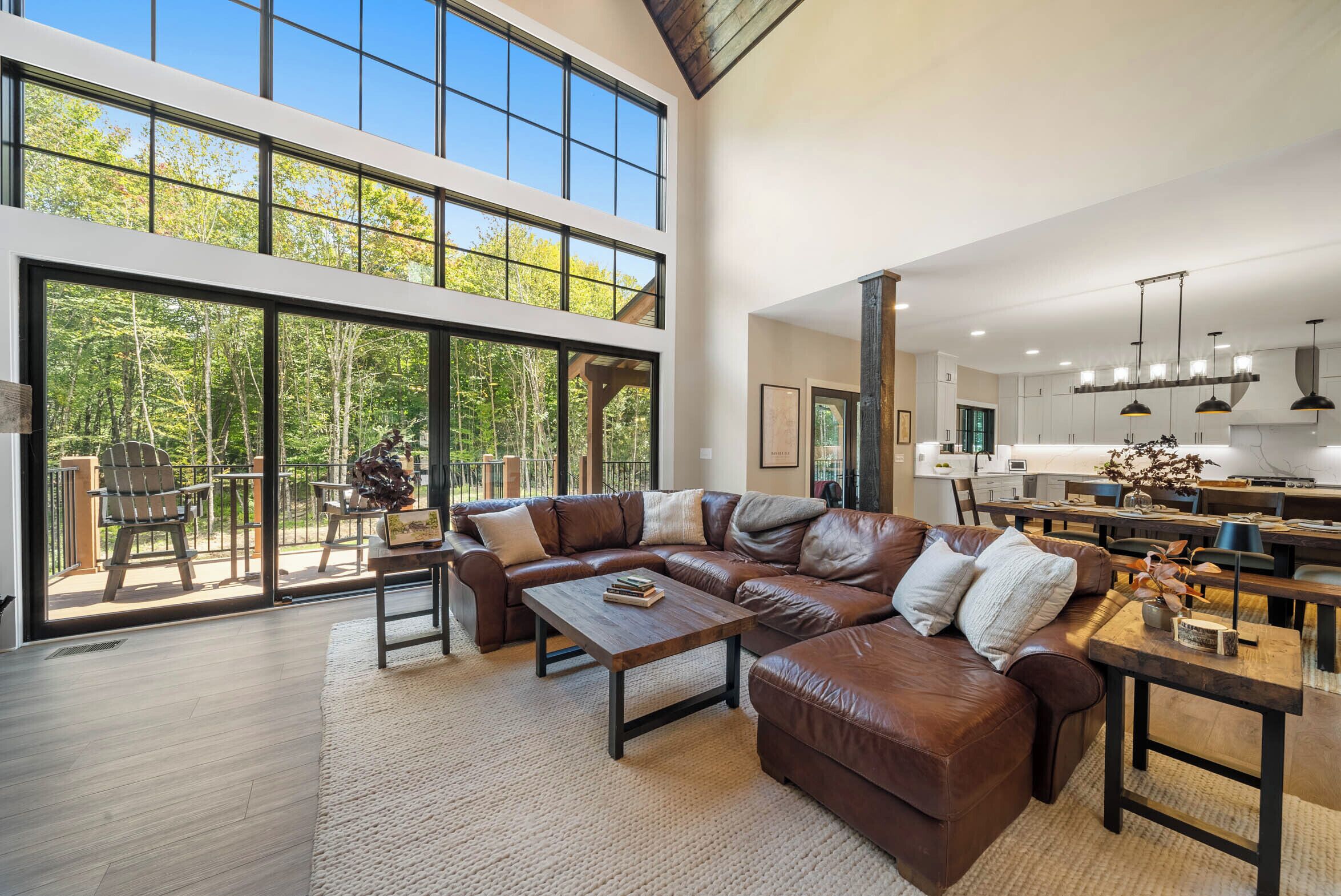 Amplia sala de estar con un sofá modular grande, una mesa de centro de madera y vistas al exterior a través de amplios ventanales.