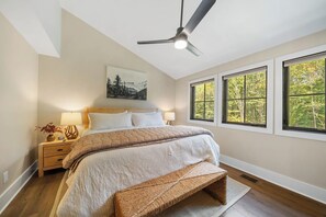 A bedroom with a bed, bedside tables, a ceiling fan, and large windows. - Creek Crossing at Eagles Nest (Banner Elk)