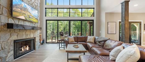 A spacious living room with a stone fireplace, leather sofa, and large windows offering a view of the outdoors.