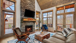 A spacious living room with a stone fireplace, large windows, and a cozy seating area.