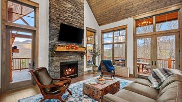 A spacious living room with a stone fireplace, large windows, and a cozy seating area.