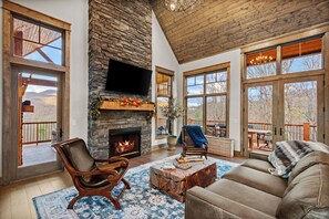 A spacious living room with a stone fireplace, large windows, and a cozy seating area. - Point of View at Eagle Bay (Butler)