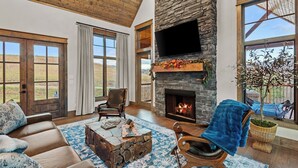 A spacious living room with a stone fireplace, large windows, and a cozy seating area.