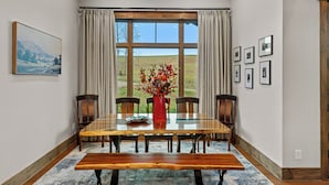 A dining area with a large table, chairs, a bench, a vase with flowers, and a painting on the wall.