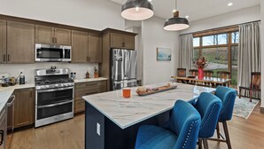 A modern kitchen with stainless steel appliances, a marble island, and blue upholstered chairs.