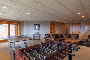 A room with a ping pong table, foosball table, leather sofa, and a small table with a bowl.