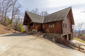 A log cabin with a steeply pitched roof, a stone foundation, and a front porch.