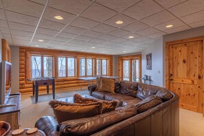 A log cabin interior with a leather sofa, wooden walls, and large windows.