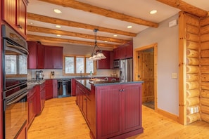 Una cocina moderna con vigas de madera, armarios rojos y electrodomésticos de acero inoxidable, además de una isla central.