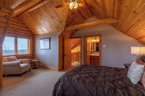 A log cabin bedroom with a large bed, a sofa, and a ceiling fan.