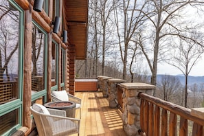 A wooden deck with stone railings, wicker chairs, and a hot tub.