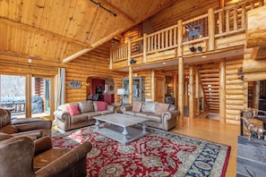 A spacious log cabin interior with a large living area, a second-floor balcony, and a rustic decor.