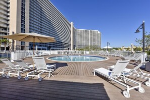 Ein Poolbereich mit Liegestühlen und Sonnenschirmen, umgeben von Hochhäusern.