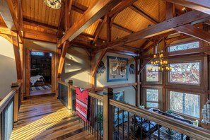 A wooden interior with a staircase leading to a loft area, a chandelier, and framed deer heads on the wall.