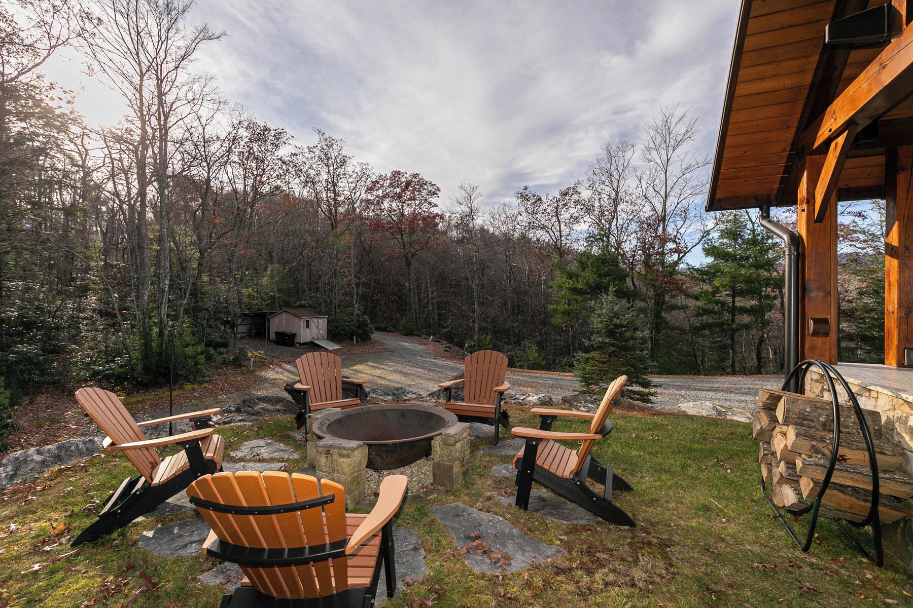An outdoor seating area with Adirondack chairs and a fire pit, surrounded by a forested landscape.