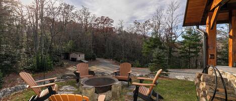 An outdoor seating area with Adirondack chairs and a fire pit, surrounded by a forested landscape.