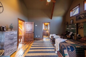 A bedroom with a wooden ceiling fan, a bed with a patterned blanket, a dresser, and a window with a view of the outdoors. - Bailey's Creek Lodge (Hudson)
