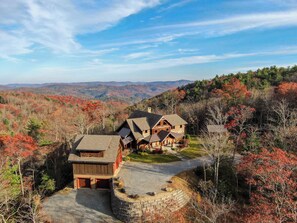 A large, rustic cabin with a stone foundation and a wooden exterior, surrounded by a stone retaining wall and a gravel driveway. - Bailey's Creek Lodge (Hudson)