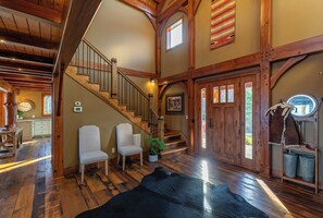 A spacious interior with a wooden staircase, a dining area, and a large black rug. - Bailey's Creek Lodge (Hudson)