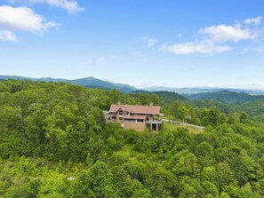A house surrounded by dense forest with a clear view of distant mountains. - Overlook at Wilderness Trail (Linville)