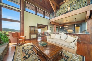 A spacious living room with a high ceiling, large windows, a cozy sofa, a wooden coffee table, and a view of the outdoors. - Overlook at Wilderness Trail (Linville)