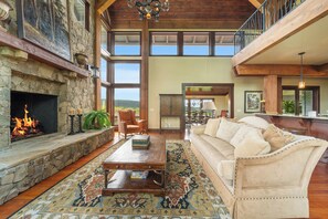 A spacious living room with a stone fireplace, a large sofa, and a coffee table. - Overlook at Wilderness Trail (Linville)