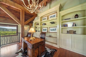 A room with a wooden desk, a chandelier, and a view of the outdoors. - Overlook at Wilderness Trail (Linville)