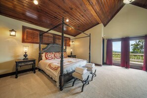Uma cama de dossel com cabeceira de madeira, duas mesas de cabeceira e vista para uma varanda com cortinas.