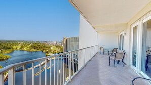 A balcony with a view of a river and cityscape, a table with chairs, and a glass door. - Laketown Wharf 1738 (Panama City Beach)