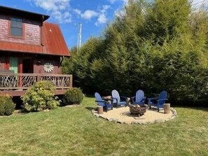 A wooden cabin with a porch and Adirondack chairs around a fire pit. - Moonlight View at Eagles Nest (Banner Elk)