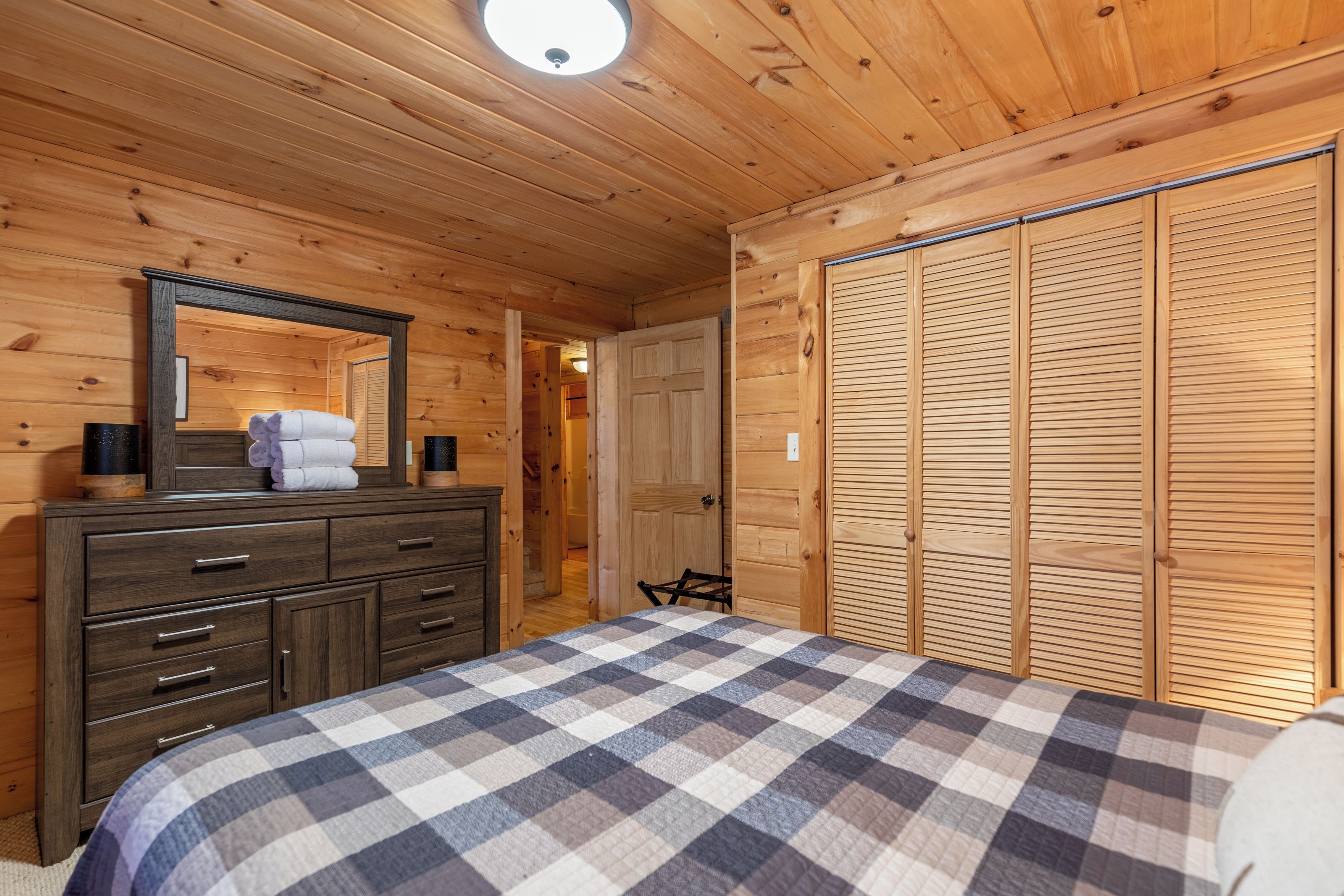 Un dormitorio con paneles de madera, una cama, cómoda, espejo y un armario amplio.