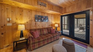 A wooden interior with a plaid sofa, two lamps, a wall-mounted sign, and a view through a glass door. - Lakeview (Vilas)