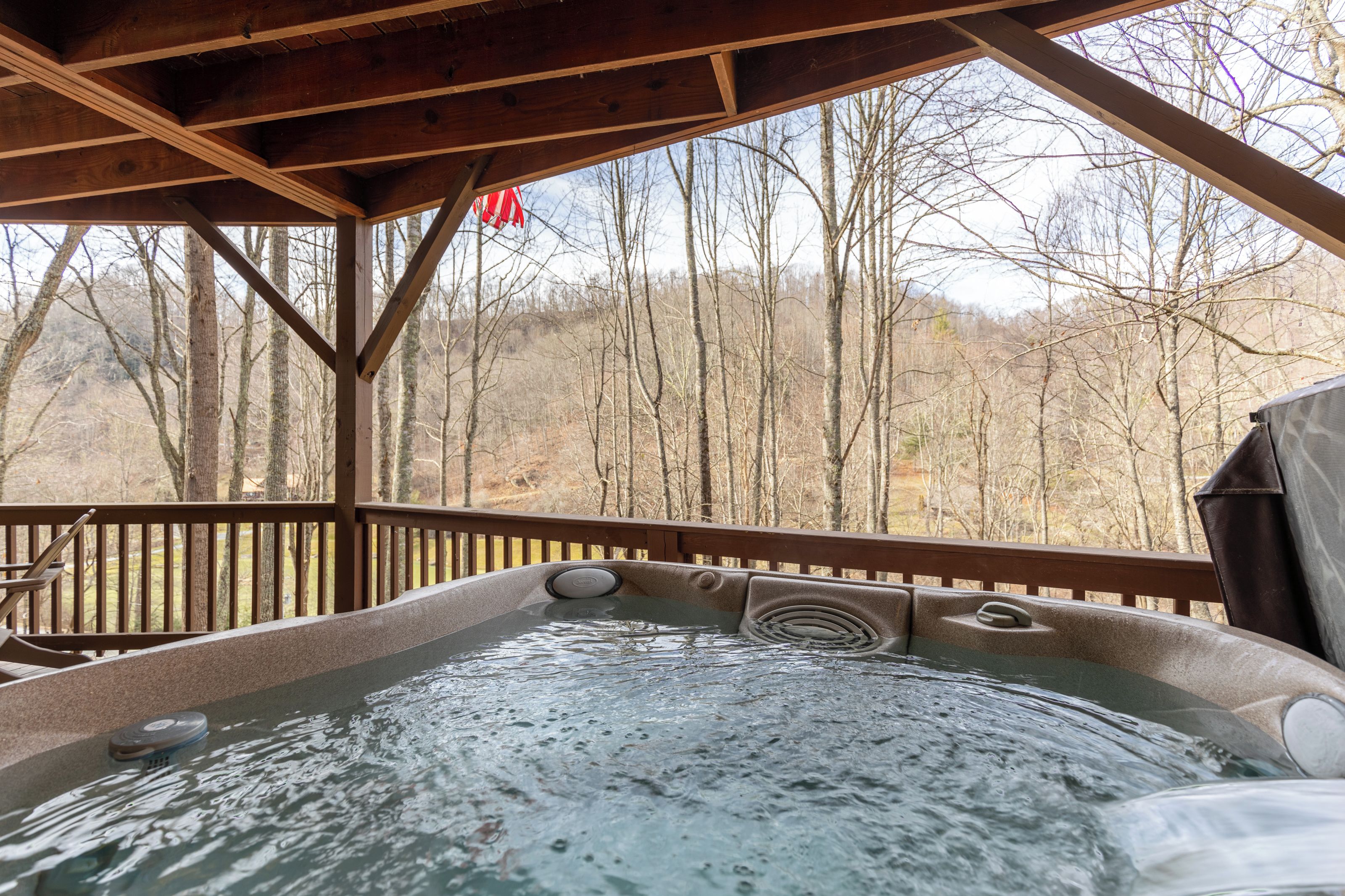 A hot tub with a wooden deck and a view of a forested area.