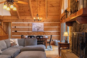 A cozy cabin interior with a wooden ceiling, a dining area, a fireplace, and a sofa with a moose pillow. - Lakeview (Vilas)
