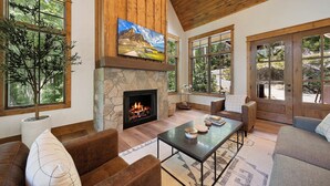 A cozy living room with a stone fireplace, wooden ceiling, large windows, and comfortable seating. - Boulder Springs Lodge at Eagles Nest (Banner Elk)