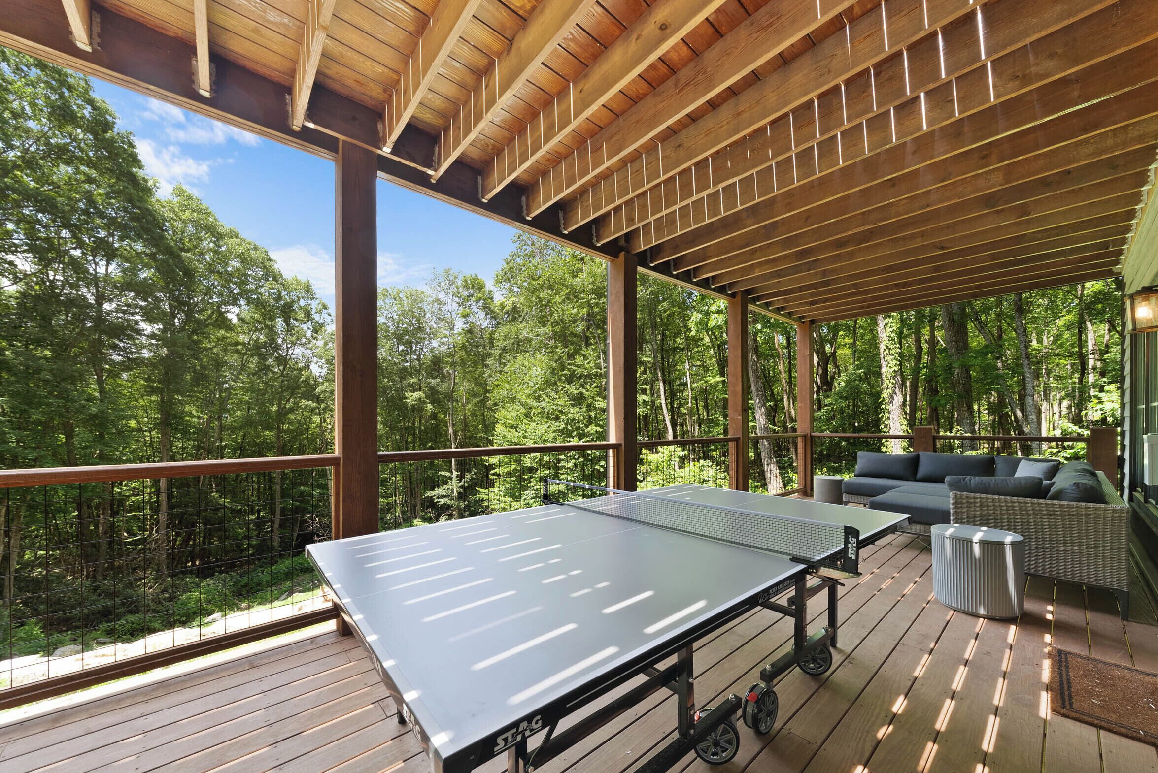 An outdoor ping pong table on a wooden deck with a view of a forest.