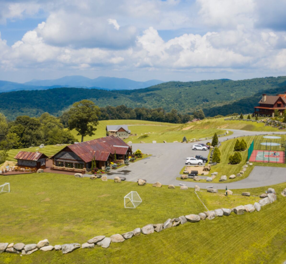 Una proprietà rurale con un'ampia area di parcheggio, diversi edifici e vista sulle montagne lontane.