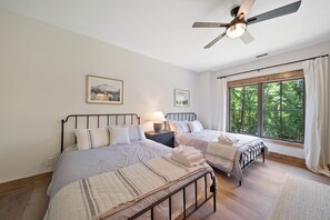 Un dormitorio con dos camas, un ventilador de techo, una ventana con cortinas e imágenes enmarcadas en la pared.