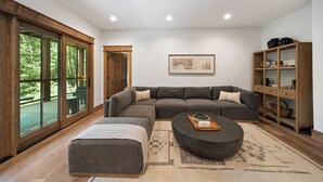 A modern living room with a sectional sofa, a round coffee table, and a bookshelf. - Boulder Springs Lodge at Eagles Nest (Banner Elk)