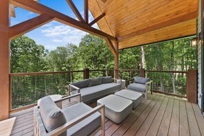 A covered outdoor seating area with a wooden deck, a sofa, and two armchairs. - Boulder Springs Lodge at Eagles Nest (Banner Elk)