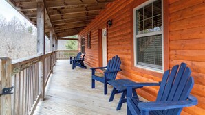 A wooden cabin with a covered porch, featuring several Adirondack chairs and a table. - Mayapple Ridge (Sugar Grove)