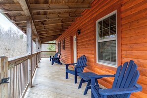 A wooden cabin with a covered porch, featuring several Adirondack chairs and a table. - Mayapple Ridge (Sugar Grove)