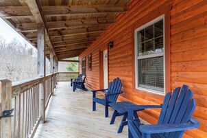 Una cabaña de madera con un porche cubierto, que incluye varias sillas Adirondack y una mesa.