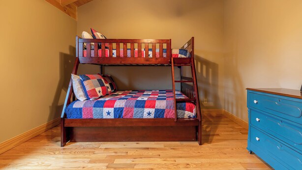 A bunk bed with a quilt, a wooden dresser, and a ceiling fan in a room with wooden flooring and walls. - Mayapple Ridge (Sugar Grove)