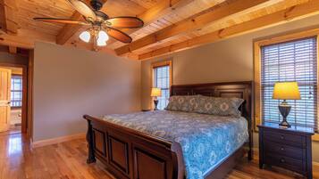 A bedroom with a wooden ceiling, a bed with a patterned bedspread, two bedside lamps, and a window with blinds.