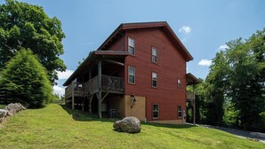 A two-story red wooden house with a balcony on the first floor, surrounded by a grassy yard and trees. - Mayapple Ridge (Sugar Grove)