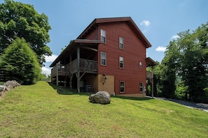 A two-story red wooden house with a balcony on the first floor, surrounded by a grassy yard and trees. - Mayapple Ridge (Sugar Grove)