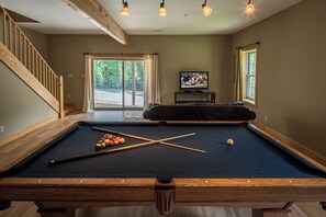 A pool table in a room with a staircase, a television, and large windows. - Mayapple Ridge (Sugar Grove)