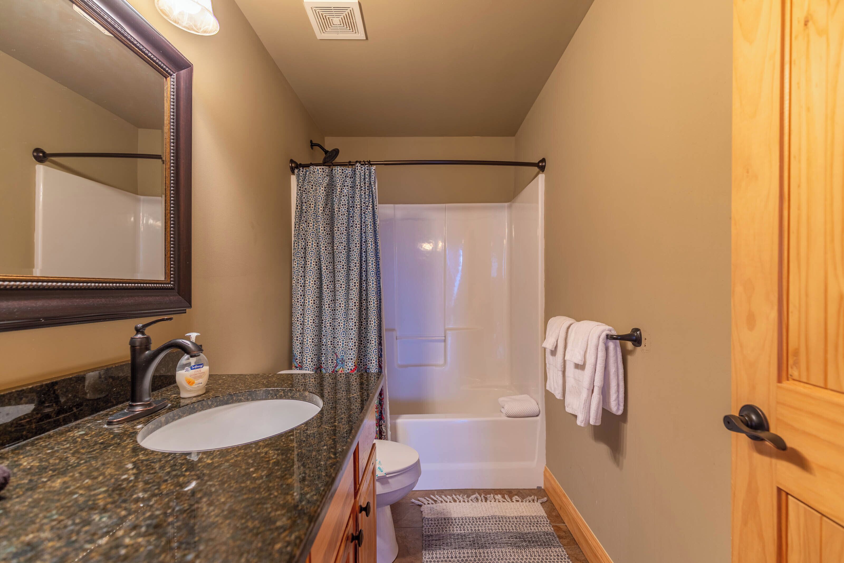 A bathroom with a granite sink, a toilet, a shower with a curtain, and a wooden door.