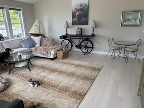 Een woonkamer met een bank, een glazen salontafel, een getextureerd vloerkleed, een kleine hond en een fiets.